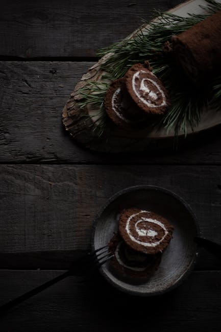 Dark and moody cake roll slices with pine leaves on a wooden background, perfect for holiday themes.