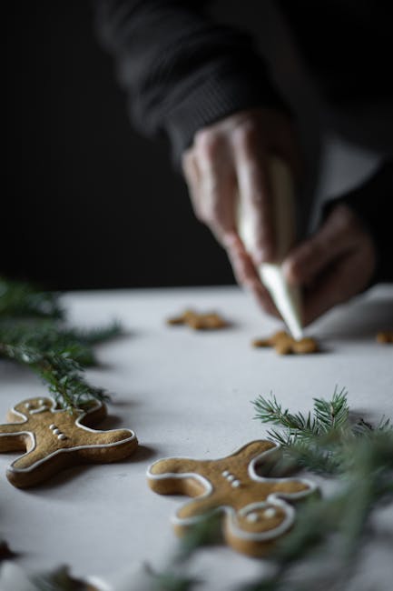 A hand decorates gingerbread men with frosting surrounded by pine leaves, creating a festive atmosphere.