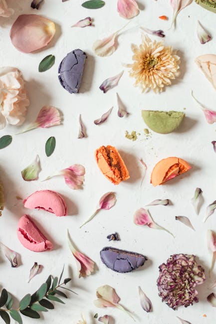 A vibrant flat lay of assorted macarons and flower petals on a white background.