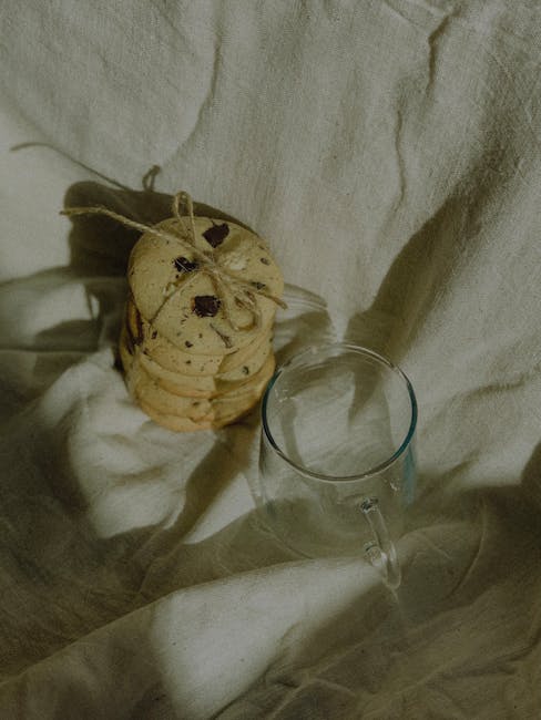 Artistic arrangement of cookies tied with twine beside a glass mug on linen fabric, creating a warm, rustic feel.