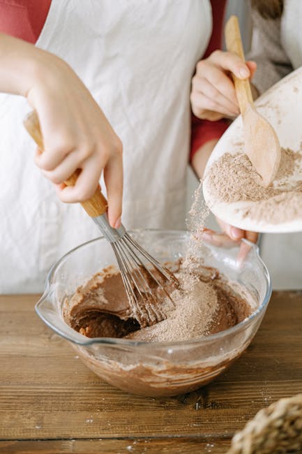 Close-up of hands mixing chocolate cake batter in a bowl, creating homemade baked goods.