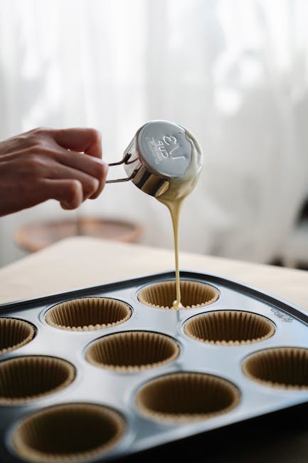 Close-up of pouring batter into muffin liners on a baking tray, indicating homemade baking.