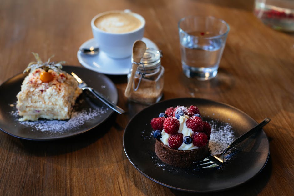A delightful setup of berry tart, cake, and cappuccino on a wooden table.