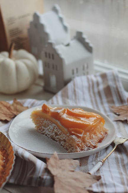 Slice of cake by window with autumn leaves and pumpkin decor.
