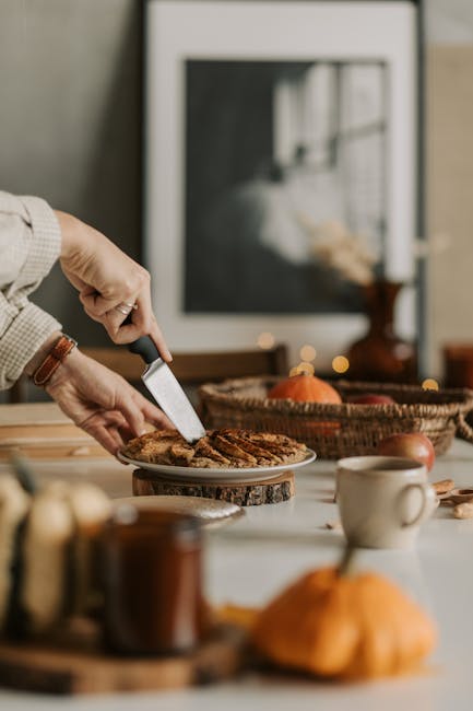 Close-up of hands slicing apple pie on a table with fall decor, creating a cozy, appetizing atmosphere.