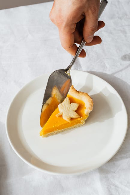 Slice of pumpkin pie with leaf decoration served on a ceramic plate, captured in natural light.